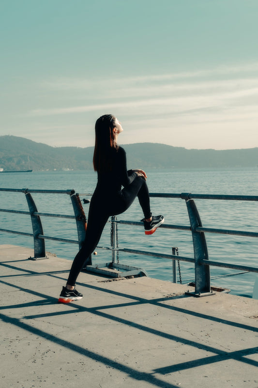 Photo by Wolrider YURTSEVEN: https://www.pexels.com/photo/woman-in-sportswear-stretching-her-legs-against-the-railing-along-the-shore-19444909/